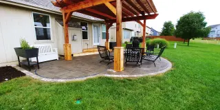 Cedar pergola built over a curved paver patio with dining and seating areas in a Johnson County backyard